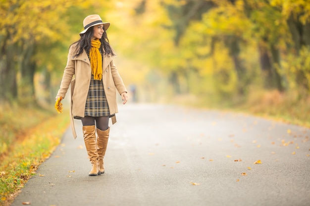 Jonge modieus geklede vrouw loopt in de kleurrijke herfstnatuur.