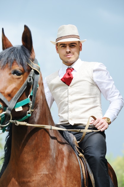 Jonge modieuze mens die berijdend een paard op platteland neemt