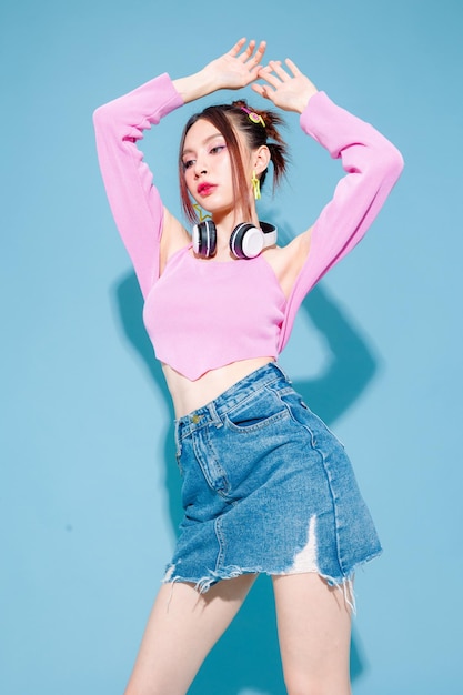 Jonge modieuze schattige zorgeloze Aziatische vrouw met hoofdtelefoon en rolschaats met perfect slank lichaam op geïsoleerde blauwe achtergrond Positief model met plezier en cool poseren binnenshuis studio