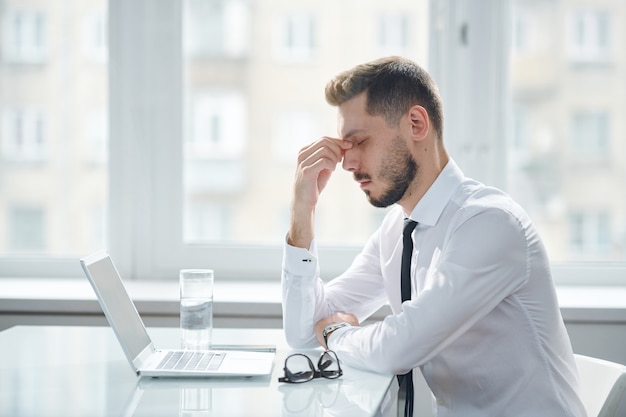 Jonge moe en gespannen manager die zich probeert te concentreren terwijl hij aan het project werkt en aan ideeën denkt