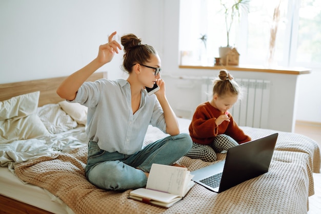 Jonge moeder die aan de telefoon praat en werkproblemen bespreekt terwijl ze voor haar kind zorgt Covid19