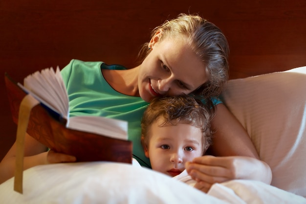 Jonge moeder die aan haar kind in bed leest