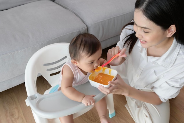 Jonge moeder die baby helpen die mengselvoedsel op kinderstoel eten