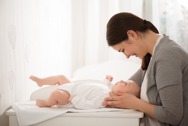 Jonge moeder die haar baby in de slaapkamer houdt.