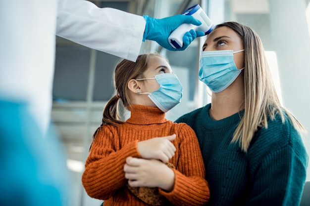 Jonge moeder die haar temperatuur laat controleren in een medische kliniek tijdens een pandemie van het coronavirus