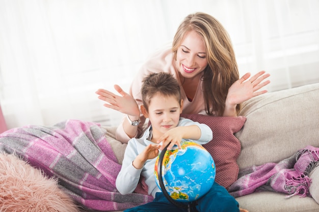 Jonge moeder die haar zoon helpt om huiswerk te doen. familie kiezen waar te reizen op vakantie. moeder en haar kind met een wereldbol