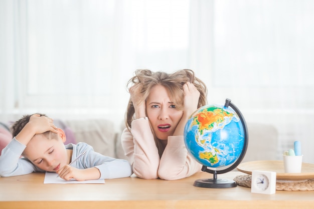 Jonge moeder die haar zoontje thuis onderwijst. moeder en haar kind studeren aardrijkskunde binnenshuis