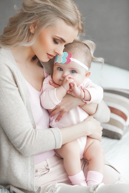 Jonge moeder die voor haar kleine babymeisje zorgt. mooie moeder en haar dochter binnenshuis in de slaapkamer. liefdevolle familie. aantrekkelijke moeder die haar kind houdt.