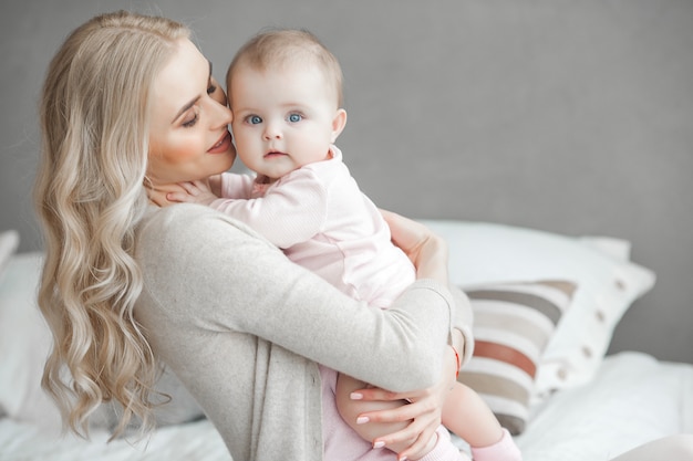 Jonge moeder die voor haar kleine babymeisje zorgt. Mooie moeder en haar dochter binnenshuis in de slaapkamer. Liefdevolle familie. Aantrekkelijke moeder die haar kind houdt.