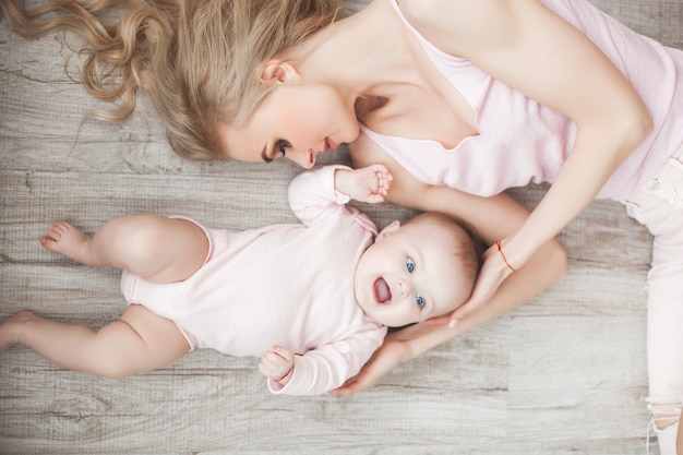 Jonge moeder die voor haar kleine babymeisje zorgt. Mooie moeder en haar dochter binnenshuis in de slaapkamer. Liefdevolle familie. Aantrekkelijke moeder die haar kind houdt.