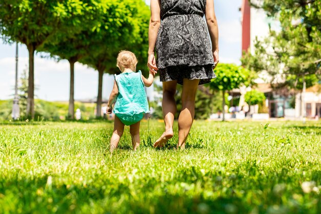 Jonge moeder en dochter op blote voeten hand in hand lopen op blote voeten op een groen gazon