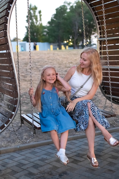 Jonge moeder en dochter op een schommel. Zomervakantie. Het concept van het opvoeden van kinderen.