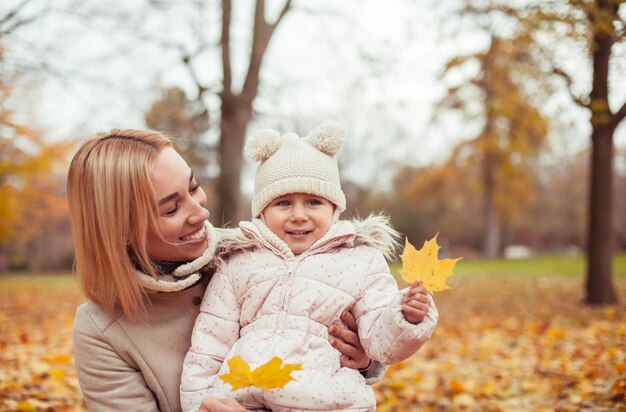 Jonge moeder en dochtertje lopen in de herfst. Moeder en dochter spelen. Warme winter. Heldere herfst. Knus.