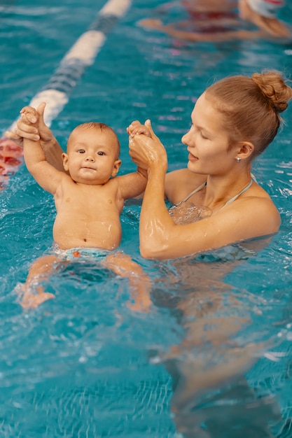 Jonge moeder en haar baby die van een babyzwemles genieten in het zwembad. Kind plezier in water met moeder