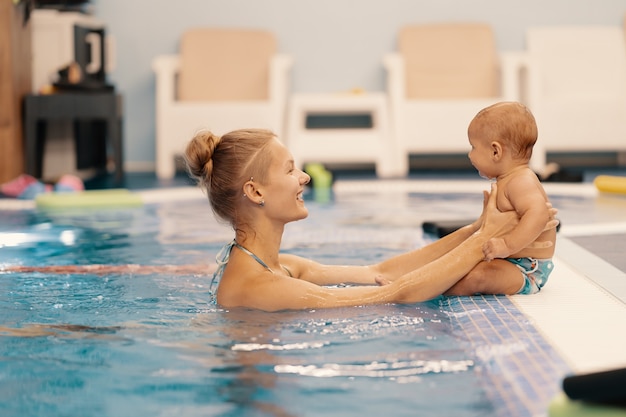 Jonge moeder en haar baby die van een babyzwemles genieten in het zwembad. Kind plezier in water met moeder