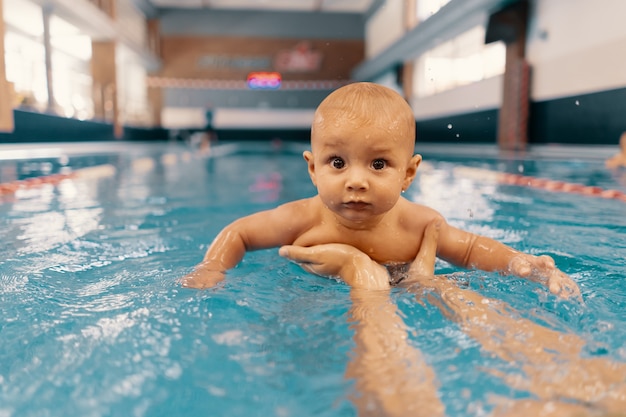 Jonge moeder en haar baby die van een babyzwemles genieten in het zwembad. Kind plezier in water met moeder