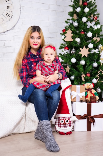 jonge moeder en haar dochter zitten in een versierde woonkamer met kerstboom