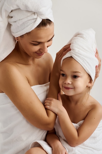 jonge moeder en haar dochtertje in witte handdoeken in de slaapkamer in de ochtend. Gelukkige familie thuis.