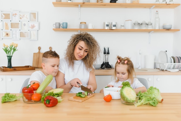 Jonge moeder en haar twee kinderen groentesalade maken