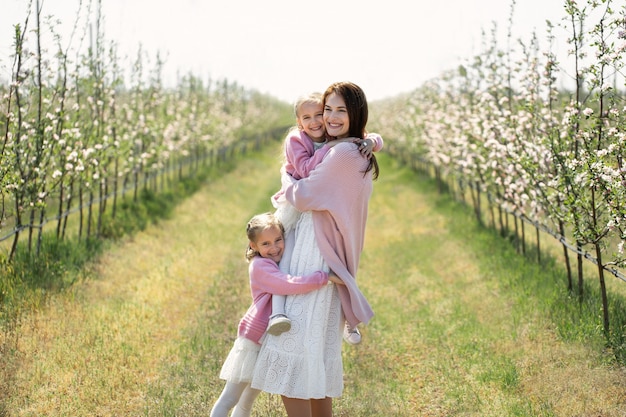Jonge moeder en haar tweelingdochters lopen in het voorjaar tijdens de bloeiperiode door een appelboomgaard en omhelzen elkaar.