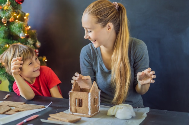 Jonge moeder en kind peperkoek huis maken op kerstavond