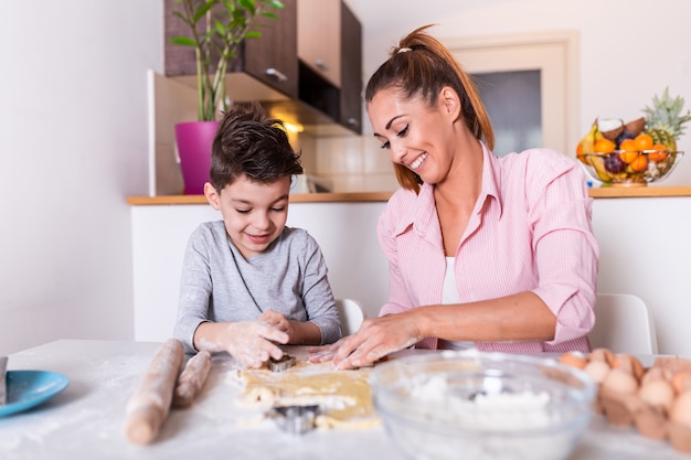 Jonge moeder en schattige zoontje jongen bereiden van het deeg, bakken koekjes en plezier in de keuken.