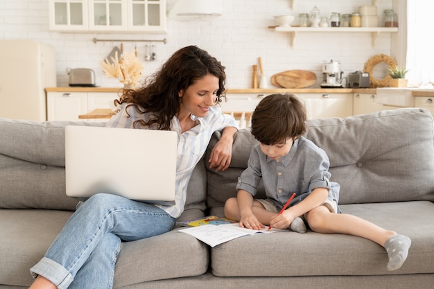 Jonge moeder externe werknemer zakenvrouw met peuter zoon op bank werken op laptopcomputer