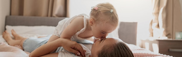 Jonge moeder glimlacht en kust haar baby terwijl ze thuis in bed ligt