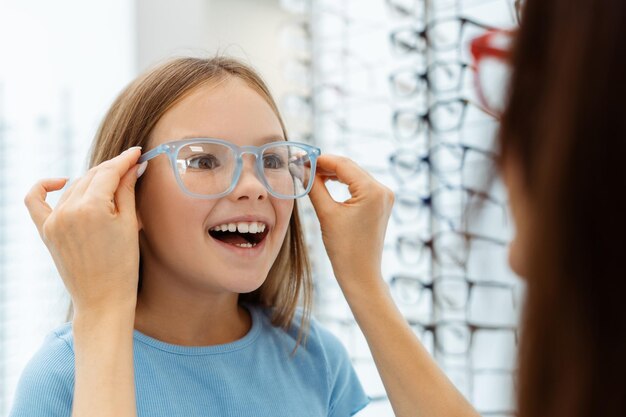 Foto jonge moeder helpt haar dochter bij het kiezen van een bril in een optische winkel gezondheidszorg gezinsconcept