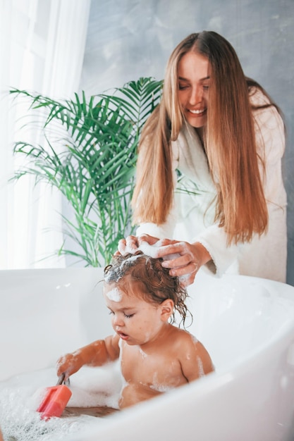 Jonge moeder helpt haar dochter zich te wassen in bad