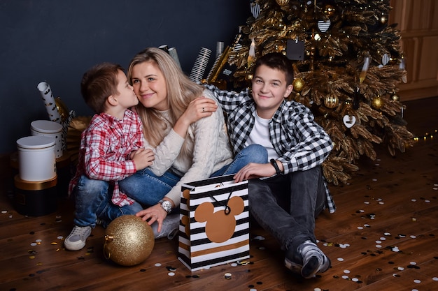 Jonge moeder in de woonkamer van het nieuwe jaar zit op de grond met geschenken en twee zonen en glimlacht