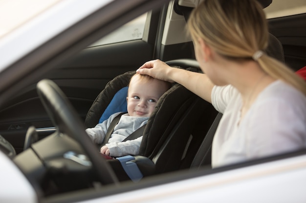 Jonge moeder kijkt naar babyjongen die in de auto in het babyzitje zit