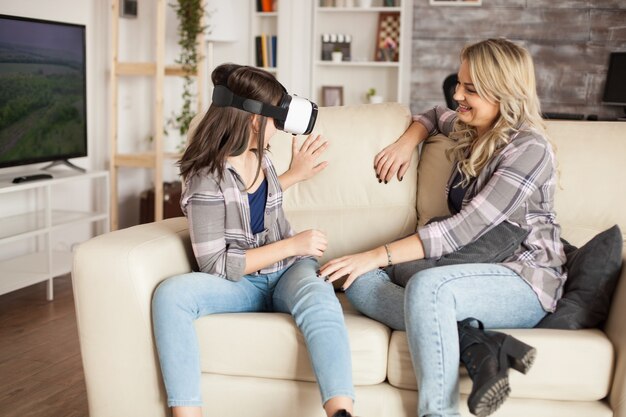 Jonge moeder kijkt naar haar kleine meisje dat plezier heeft met virtual reality-headset. Modern moederschap.