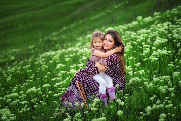 Jonge moeder knuffelt haar dochter terwijl ze op een weide met bloeiende bloemen zit