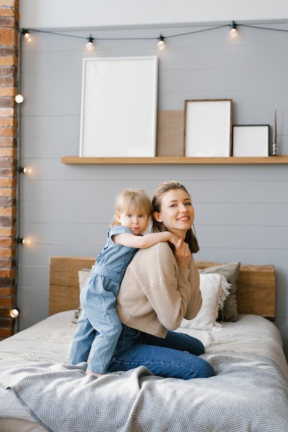 Jonge moeder knuffelt met haar tweejarige dochtertje op bed