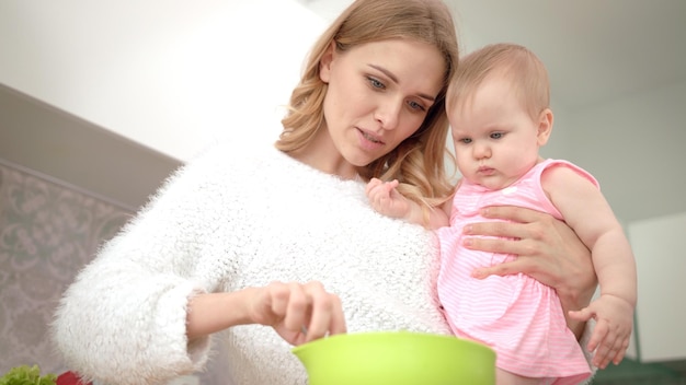 Jonge moeder koken met baby op handen Babyvoeding koken
