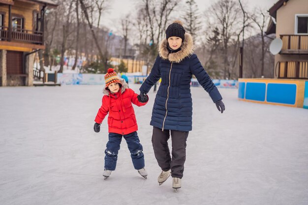 Foto jonge moeder leert haar kleine zoon schaatsen op een schaatsbaan. het gezin geniet van de winter op de schaatsbaan buiten.