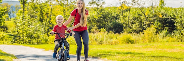 Jonge moeder leert haar zoon fietsen in het lange formaat van de parkbanner