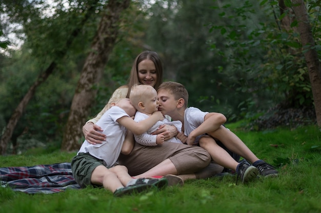 Jonge moeder met drie kleine kinderen die in de zomer picknicken. Grote neef knuffel en kus haar jongere zus.