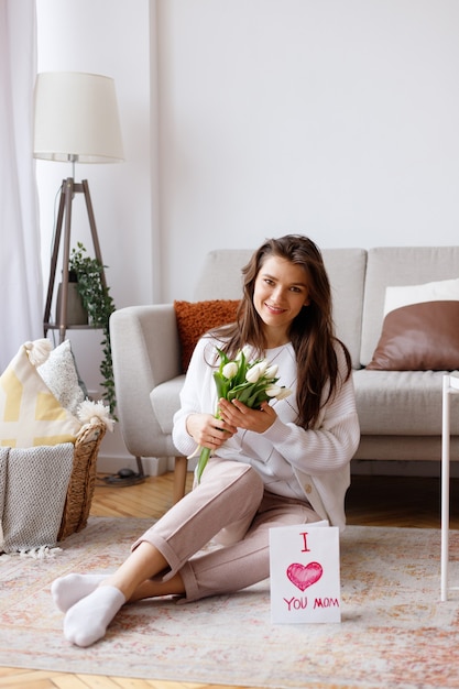 Jonge moeder met een boeket tulpen en een ansichtkaart in de woonkamer