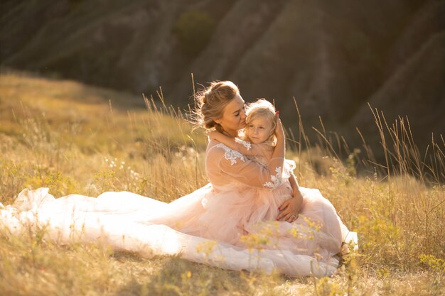 Jonge moeder met een dochtertje in roze jurken zit in het veld