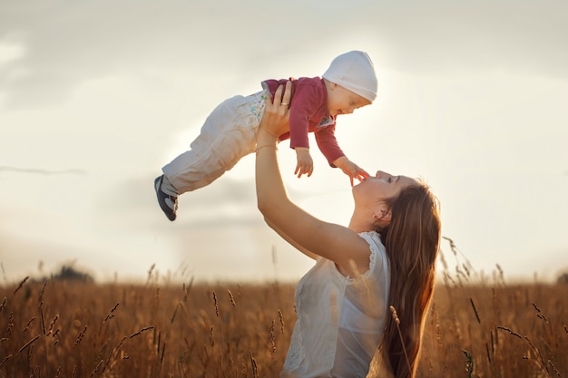 Jonge moeder met haar schattige kind, moeder gooit baby, lachen en spelen in de zomer op de aard.