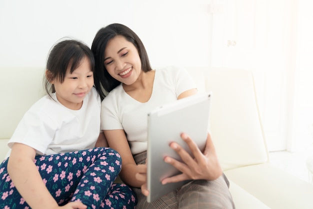 Jonge moeder met kinderen die digitale tablet samen thuis gebruiken. glimlachend gezin kijken naar scherm, speelgoed winkelen of cartoon online kijken,