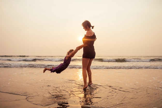 Jonge moeder met klein meisje op haar rug op het strand in de zomer Gelukkige familie die leuke zomervakantie heeft