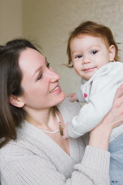 Jonge moeder met kleine kinderen op handen die op bank zitten. Jonge vrouw met dochter