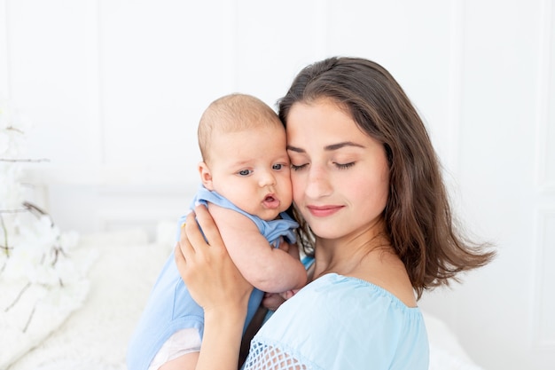 Jonge moeder met pasgeboren baby knuffelt thuis op het bed, gelukkige familie en verjaardagsconcept.