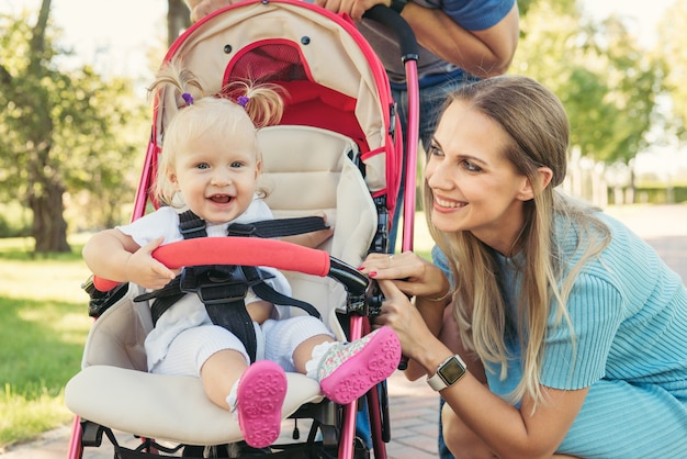 Jonge moeder praten met lachende baby in roze kinderwagen. ouders buiten lopen met kind