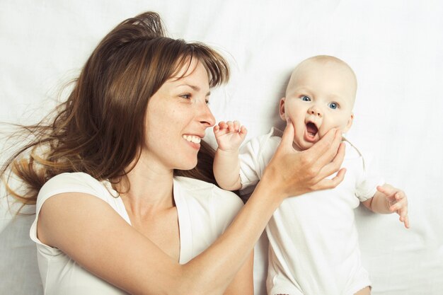 Jonge moeder speelt met haar baby op een bed met een wit laken.