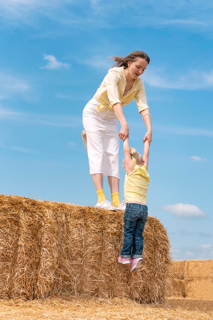 Jonge moeder speelt met klein kind op boerderij in droog hooi Moeder en dochter op hooiberg Blauwe lucht Zomerdag