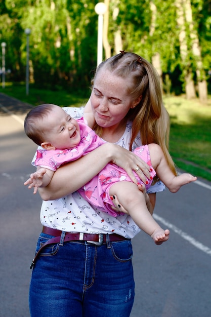 Jonge moeder spelen en lachen baby in groen park.